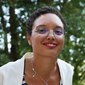 Portrait d'une femme souriante avec lunettes dans un parc verdoyant, évoquant bien-être et confiance pour l'optique et la santé visuelle.